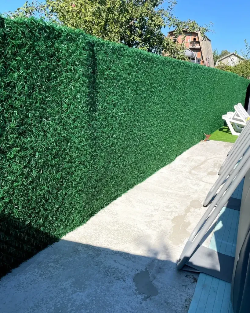 Світло зелена декоративна огорожа із штучної хвої на сітці рабиця біля будинку